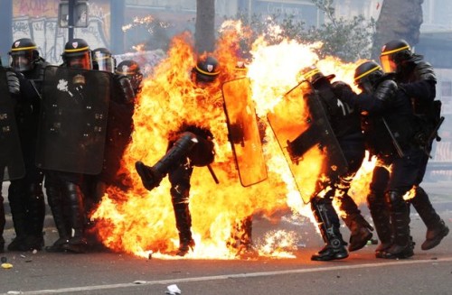 Un agente della Gendarmerie è completamente circondato dalle fiamme, mentre la violenza aumenta